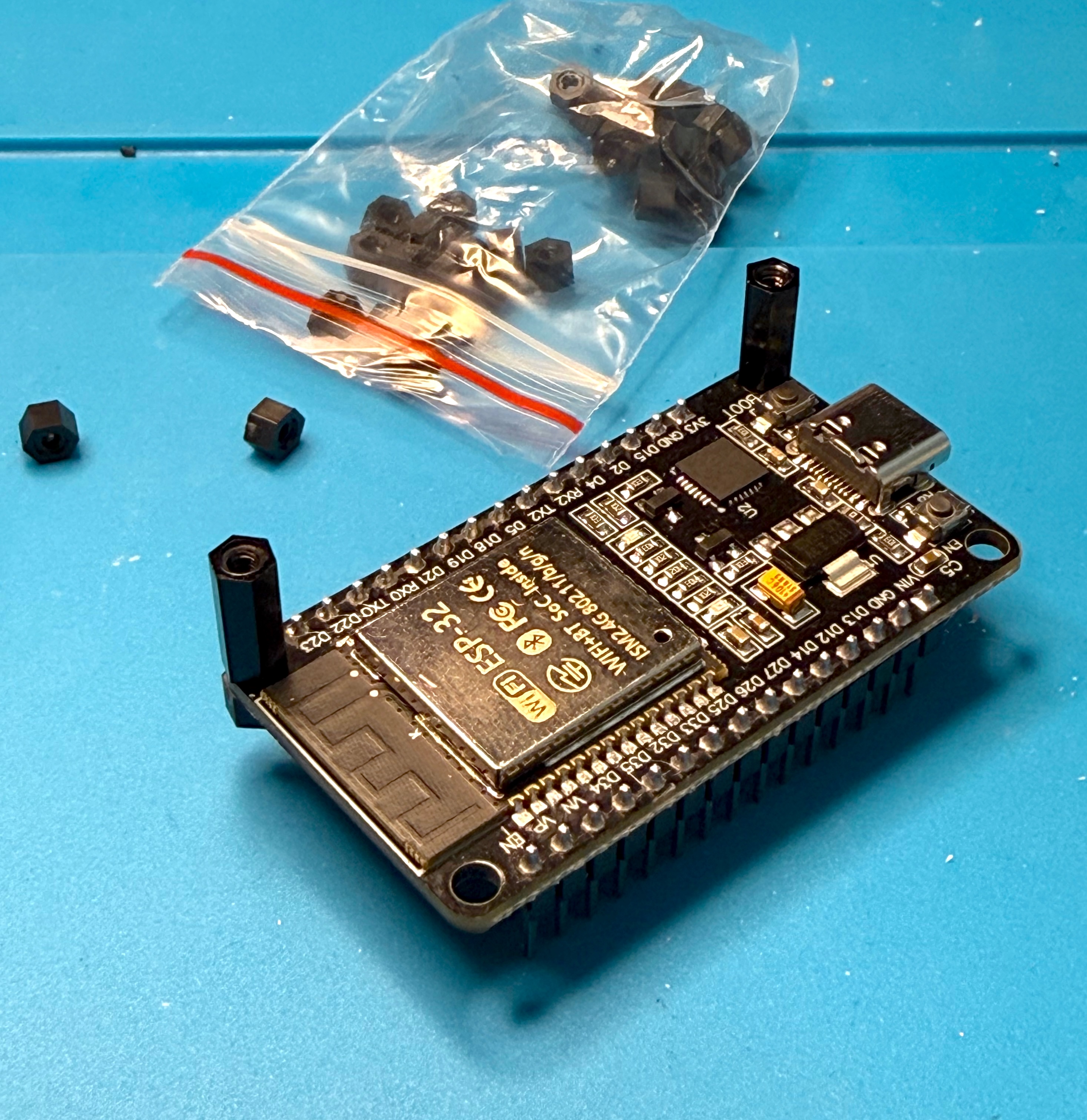 The ESP32 board with two black standoffs fitted, next to a bag of spares