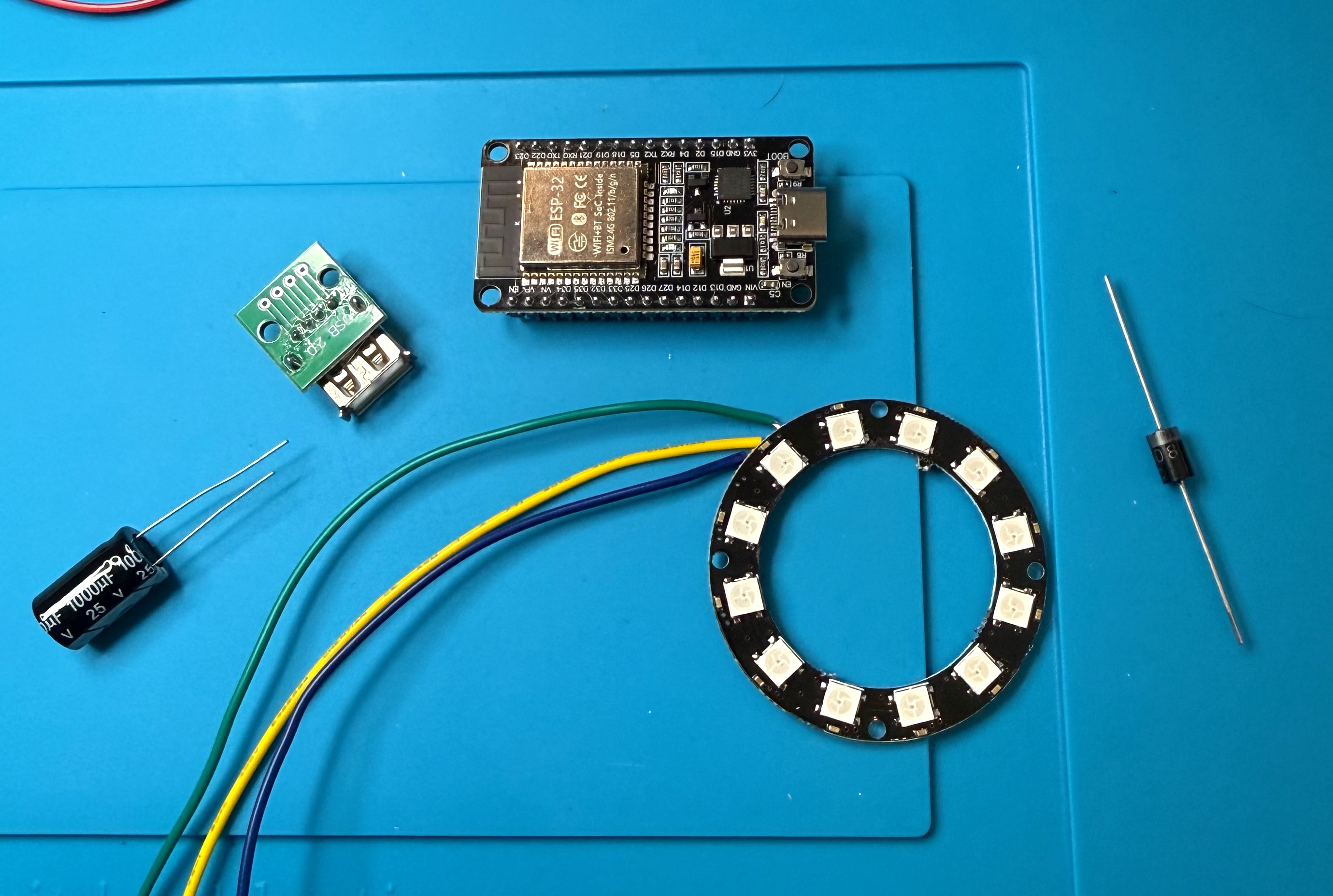 ESP32-WROOM-32 board, 12-LED WS2812 ring, USB-A breakout, 1N5408 diode, 1000 µF capacitor and hook-up wire laid out on a bench mat
