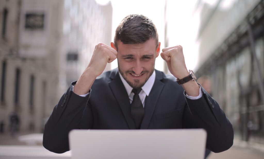 A man in front of a laptop, looking happy for achieving something.